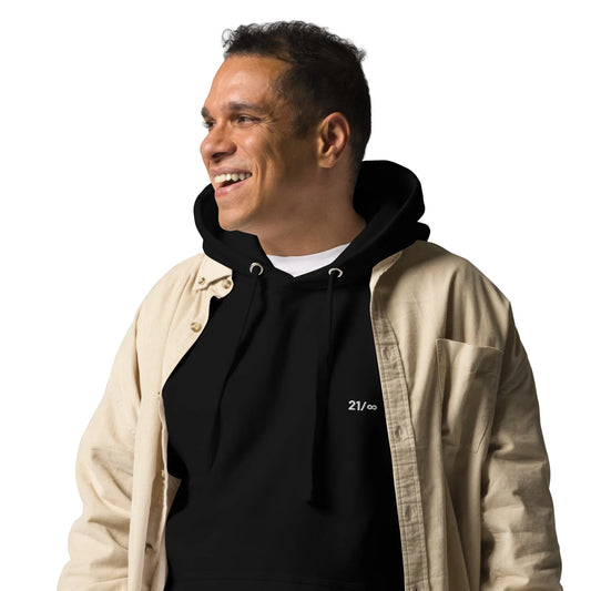 Lächelnder Mann in schwarzem Hoodie mit weißem 21/∞ Logo und offener beiger Jacke vor weißem Hintergrund